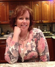 woman in the kitchen wearing a floral top smiling