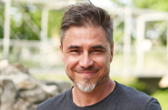 a bearded man wearing a dark grey shirt, smiling