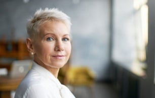 woman with pixie cut hair with blue eyes wearing a white top smiling