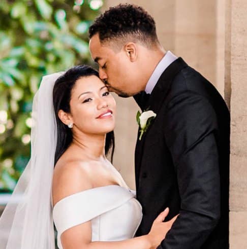 tall and handsome groom kissing his smiling bride wearing a white bridal gown on the forehead